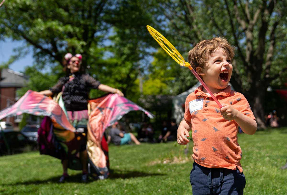 A young boy smiling holding a bubble wand in front of a woman dancing.