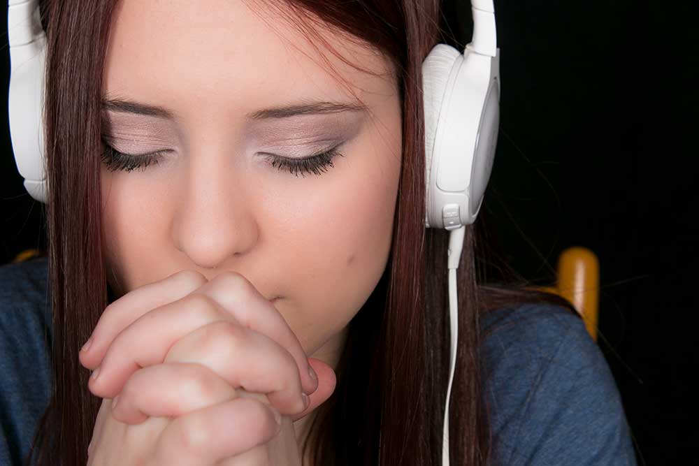 Closeup of a young woman praying while wearing white headphones