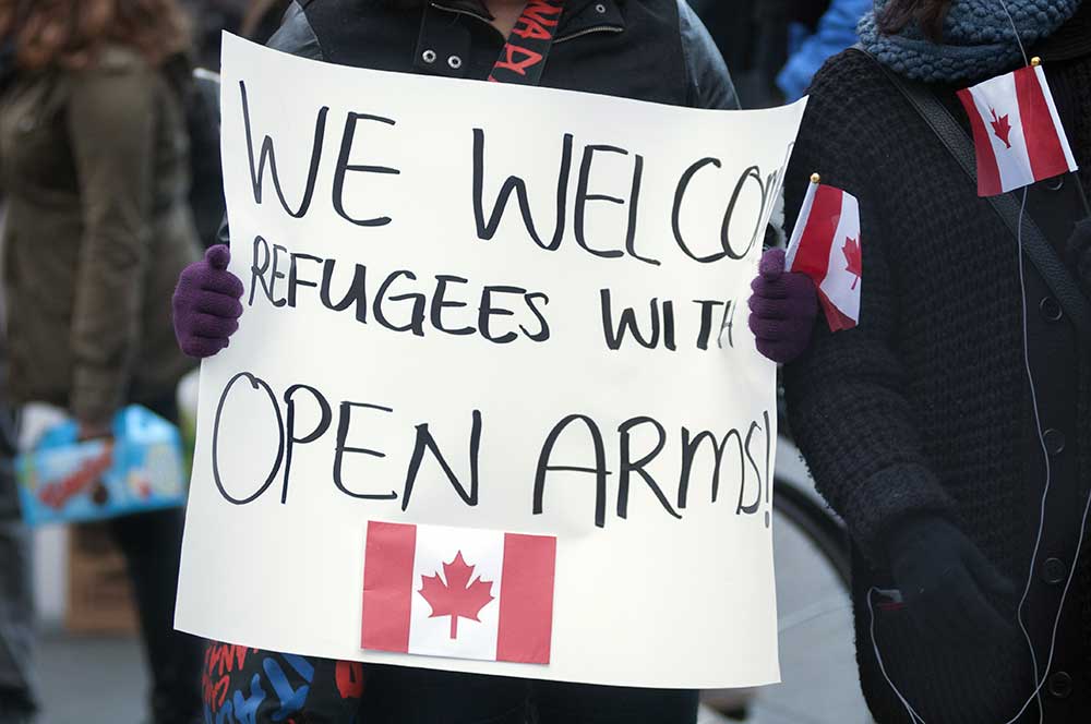 Detail of a hand drawn sign that says We Welcome Refugees With Open Arms above a drawing of the Canadian Flag
